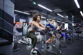 Young people doing exercises on elliptical trainer in gym�