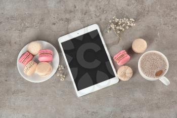 Flat lay composition with tasty macarons, cup of coffee and tablet computer on grey background�