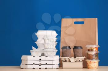 Different packages with delicious food on table against color background. Delivery service�