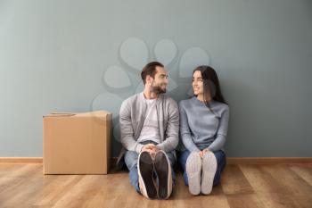 Young couple sitting on floor near box indoors. Moving into new house�