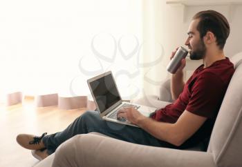 Male freelancer drinking beer while working with laptop in home office�