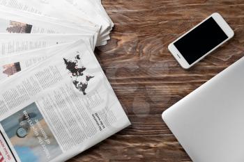 Morning newspapers and mobile phone on wooden table�