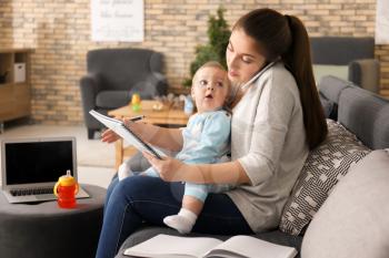 Young mother holding baby while working at home�