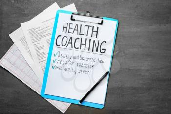 Health coaching written on sheet of paper with medical documents on grey background�