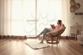 Young woman reading interesting book at home�