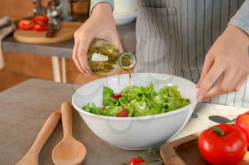 Woman adding olive oil into bowl with fresh vegetable salad on table�