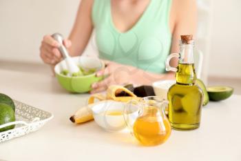 Woman making nourishing mask with avocado in kitchen�