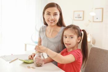 Little girl with her mother sitting at table and counting money indoors. Money savings concept�