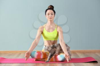 Beautiful woman with cat practicing yoga indoors�