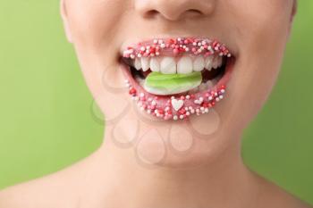 Beautiful young woman with creative makeup and candies in mouth on color background, closeup�