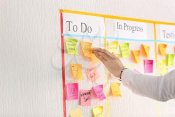 Man attaching sticky note to scrum task board in office�
