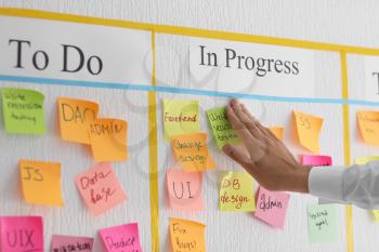 Man attaching sticky note to scrum task board in office�