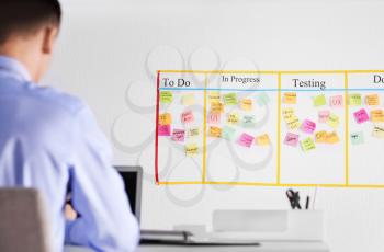 Man working in office with scrum task board on wall�