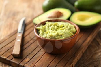 Bowl with tasty guacamole and ripe avocado on wooden board�