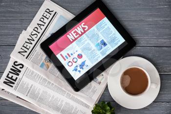 Tablet computer with news on screen and newspapers on wooden background�