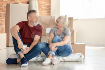 Mature couple with moving boxes sitting on carpet at new home�