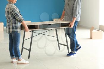 Mature couple carrying table in room after moving to new home�