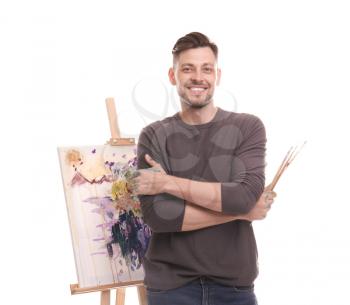Male artist with paintbrushes near easel on white background�