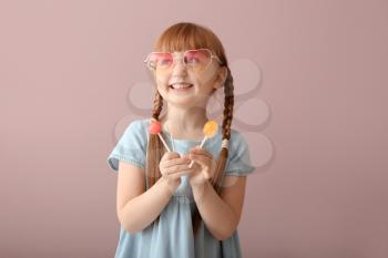 Cute little girl with lollipops on color background�
