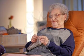 Senior woman knitting in armchair at home�