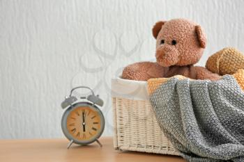 Wicker basket with plaid, funny toy and alarm clock on table against light background�