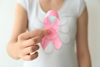 Woman holding pink ribbon on light background, closeup. Breast cancer awareness concept�