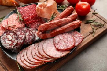 Plate with assortment of delicious deli meats on wooden board�