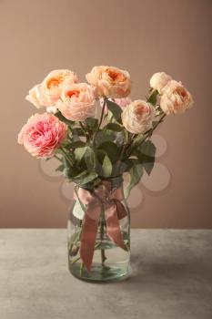 Vase with bouquet of beautiful roses on table against color background�
