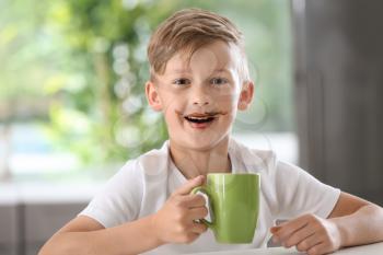Cute little boy with cup of hot cocoa drink at table�