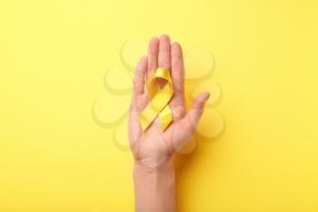 Female hand holding yellow ribbon on color background. Cancer concept�