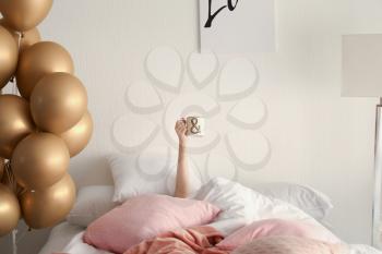 Woman holding cup in bed with beautiful air balloons at home�