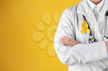 Doctor with yellow ribbon on robe against color background. Cancer awareness concept�