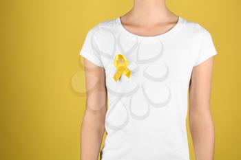 Woman with yellow ribbon on color background. Cancer awareness concept�