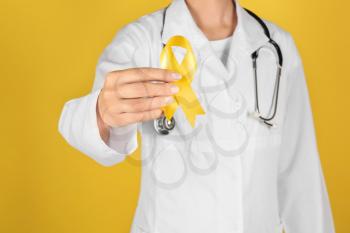 Doctor with yellow ribbon on color background. Cancer awareness concept�