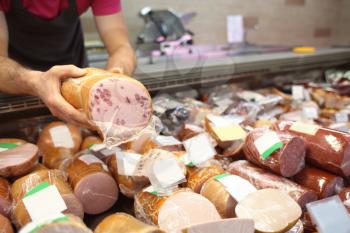 Male seller holding piece of deli meat in butcher shop�