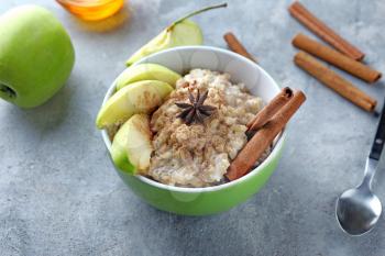 Bowl with tasty oatmeal, sliced apple and spices on grey textured background�