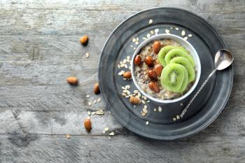 Bowl with tasty oatmeal, sliced kiwi and nuts on wooden table�
