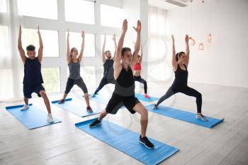 Group of sporty people practicing yoga indoors�