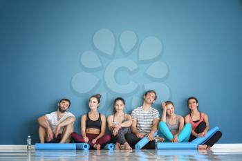Group of people with yoga mats sitting on floor near color wall�