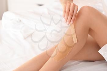 Young woman epilating her leg with liquid sugar on bed, closeup�