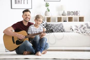 Father teaching his son to play guitar at home 