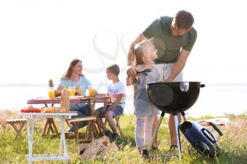 Young man with daughter cooking tasty food on barbecue grill outdoors. Family picnic�