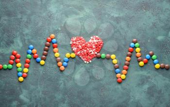 Composition with tasty candies in shape of pulse and heart on color background�