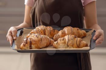 Young woman holding baking tray with fresh croissants indoors�