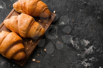 Board with tasty croissants on grey textured background�