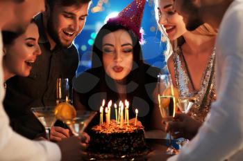 Young woman blowing out candles on her birthday cake with friends in club�