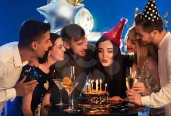 Young woman blowing out candles on her birthday cake with friends in club�
