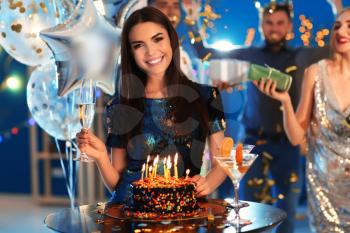 Young woman near her birthday cake at party in club�