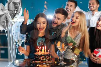 Young woman with friends near her birthday cake at party in club�
