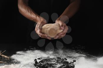 Man holding raw dough on black background�